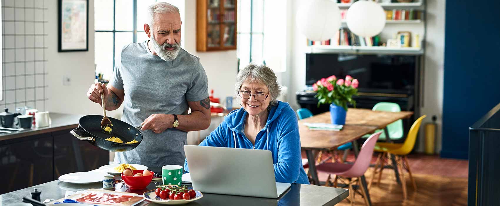 Man cooking while woman is using laptop.