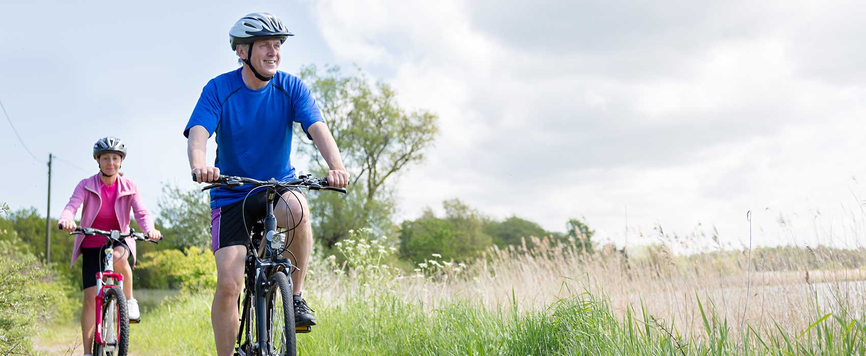 Man and woman riding bicycles through a field.