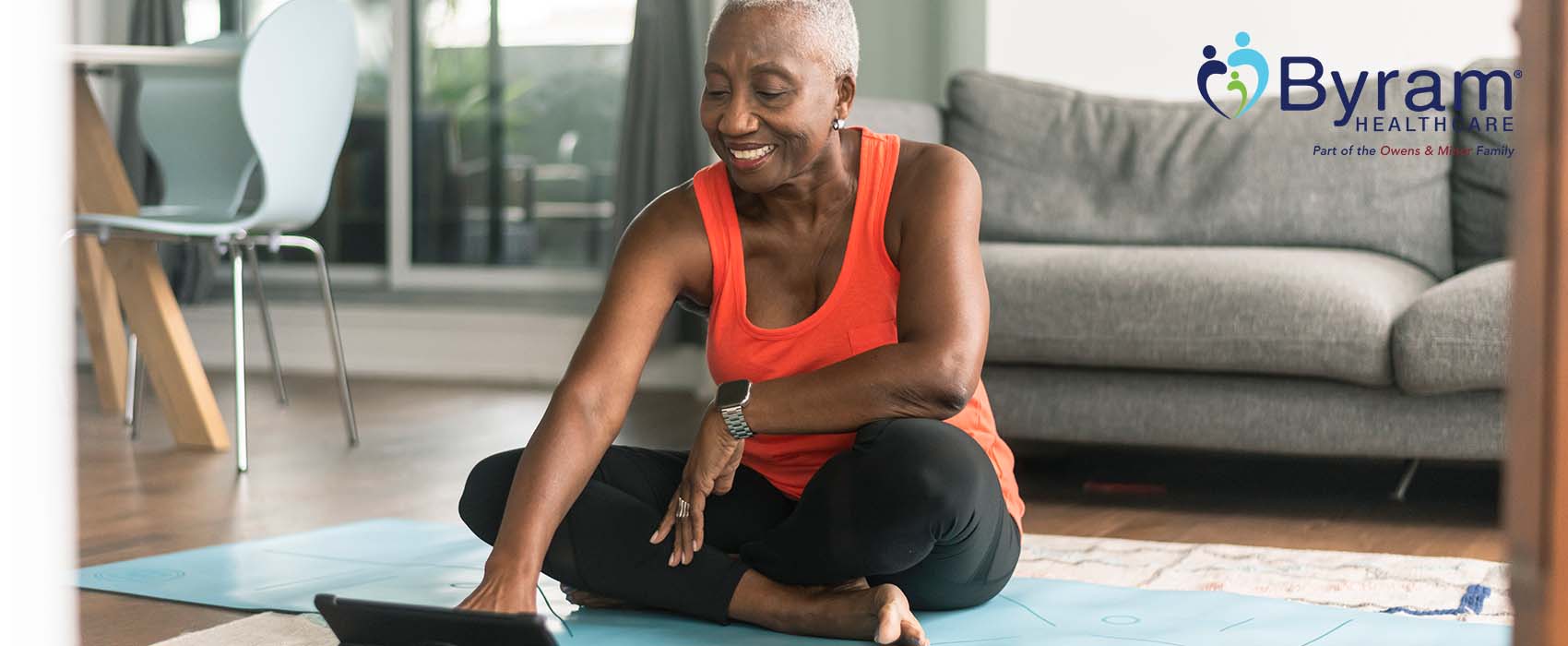 Woman sitting on a yoga mat looking at a laptop.