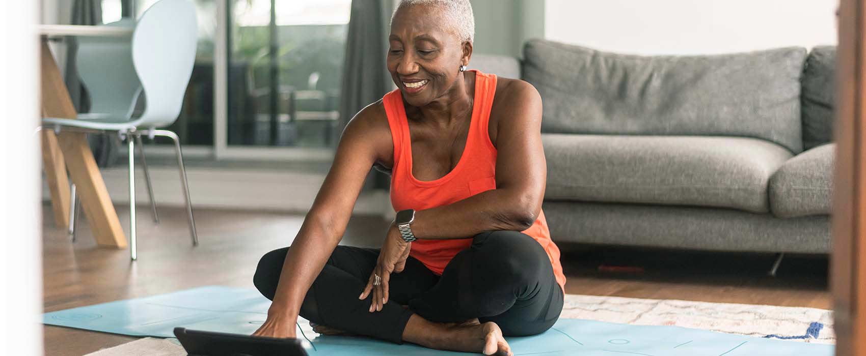 Woman sitting on a yoga mat looking at a laptop.