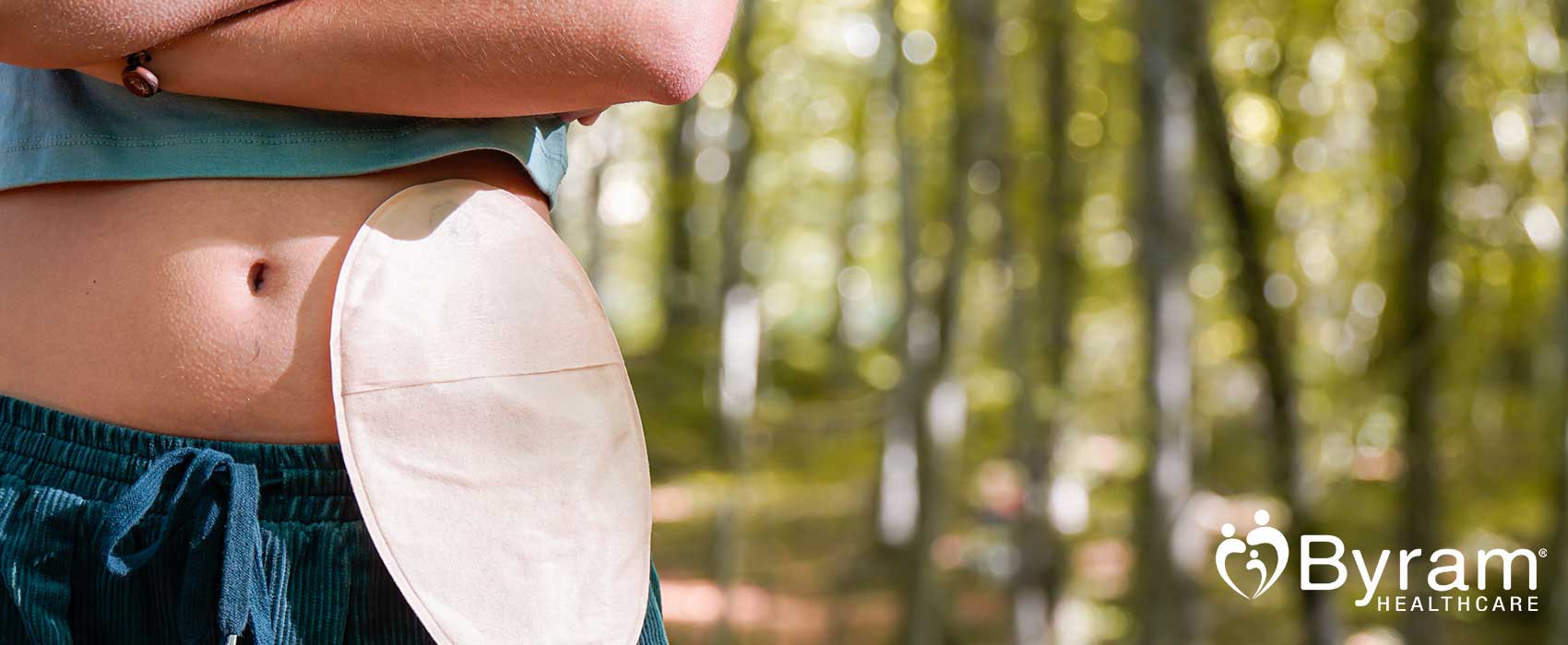 Woman with an ostomy pouch standing in a forest.