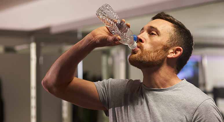 Hombre bebiendo una botella de agua en el gimnasio.