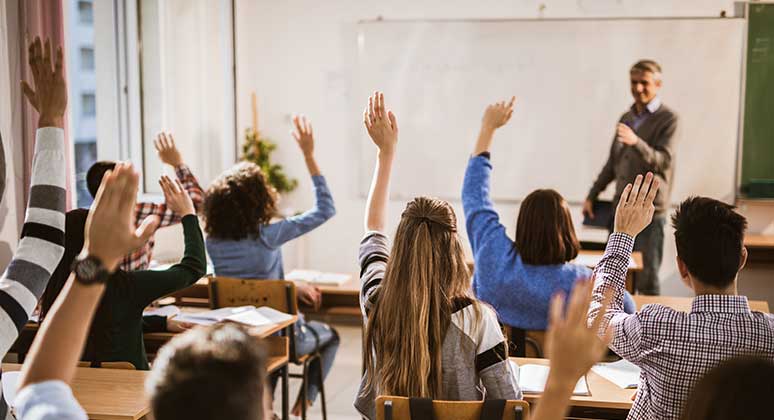 Kids in a classroom raising their hands.