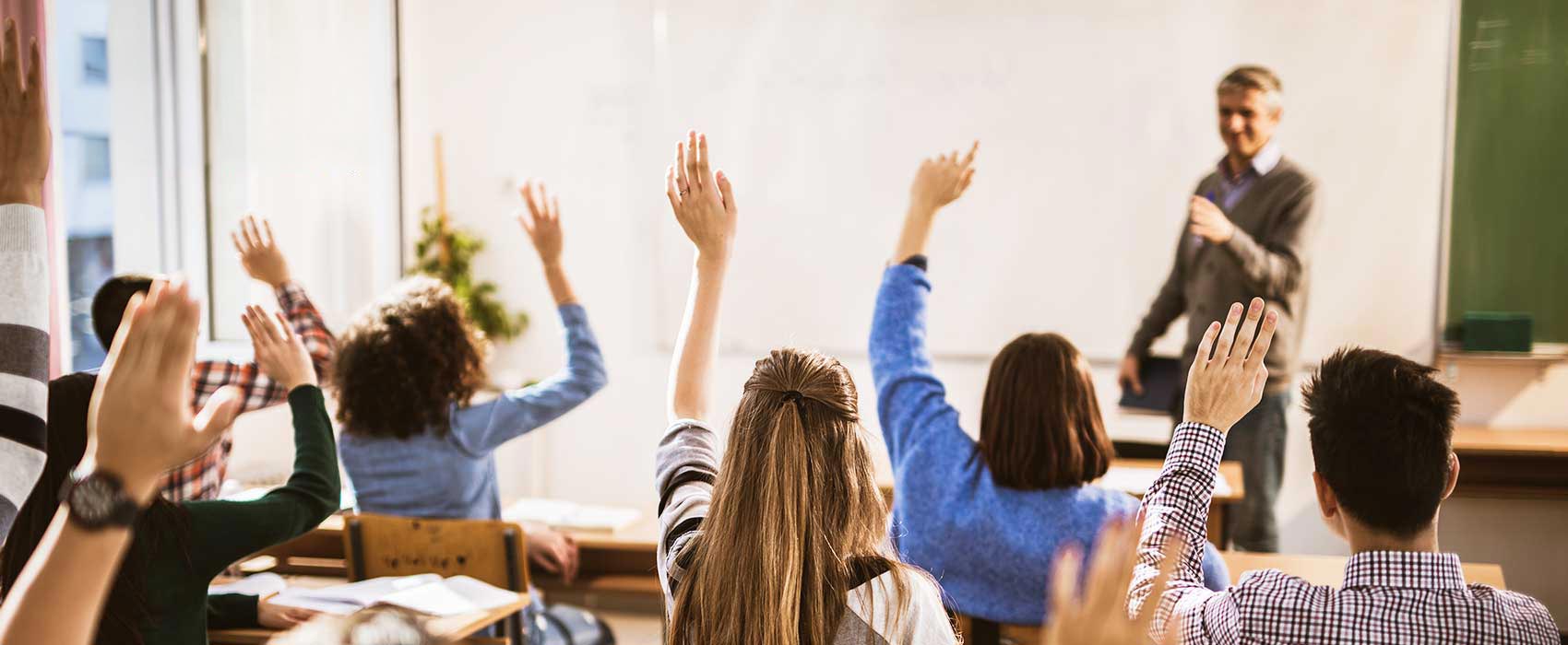Kids in a classroom raising their hands.