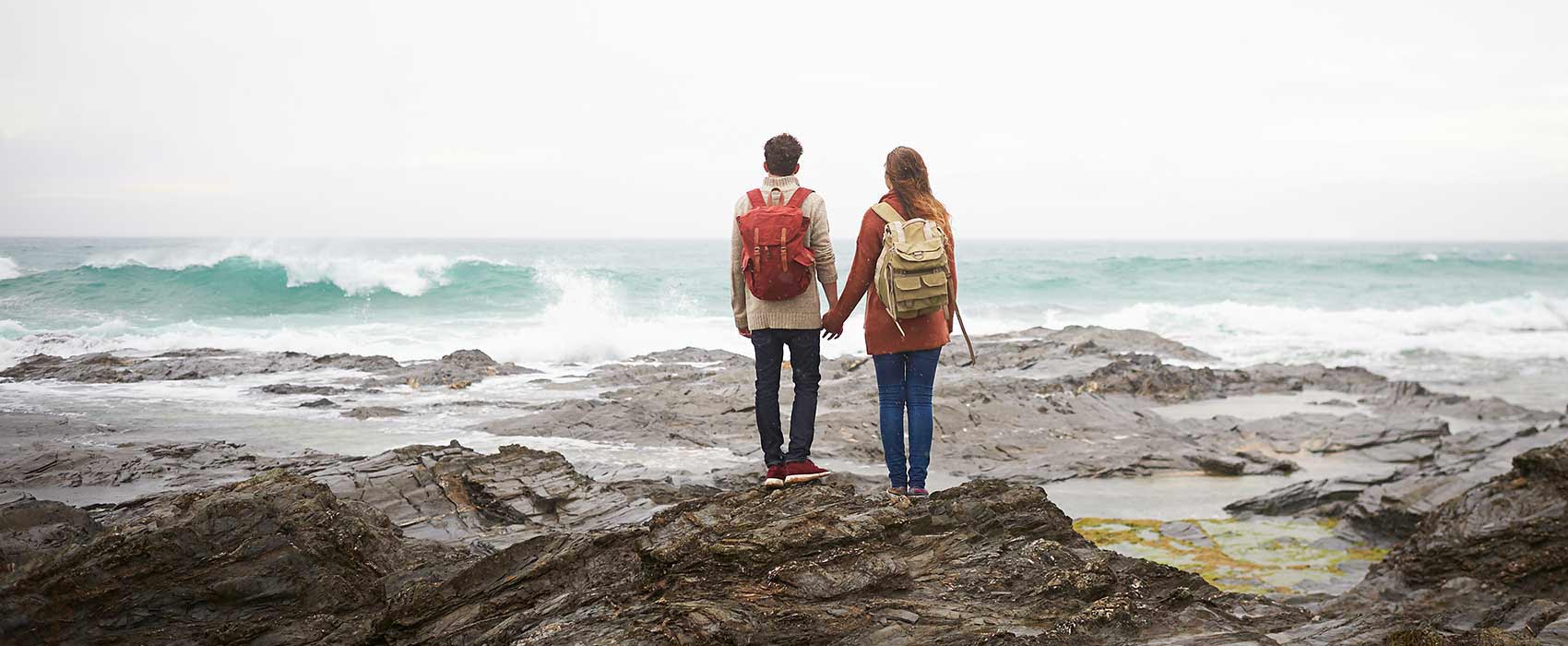 Couple holding hands on beachy rocks.