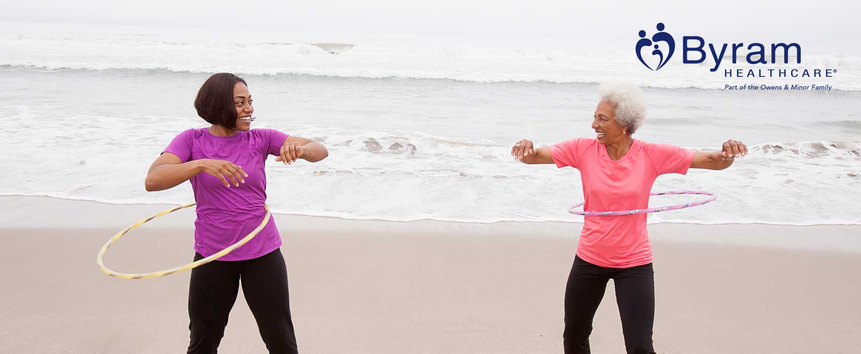 Two women hula hooping on the beach.