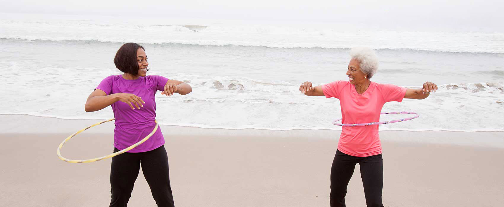 Two women hula hooping on the beach.