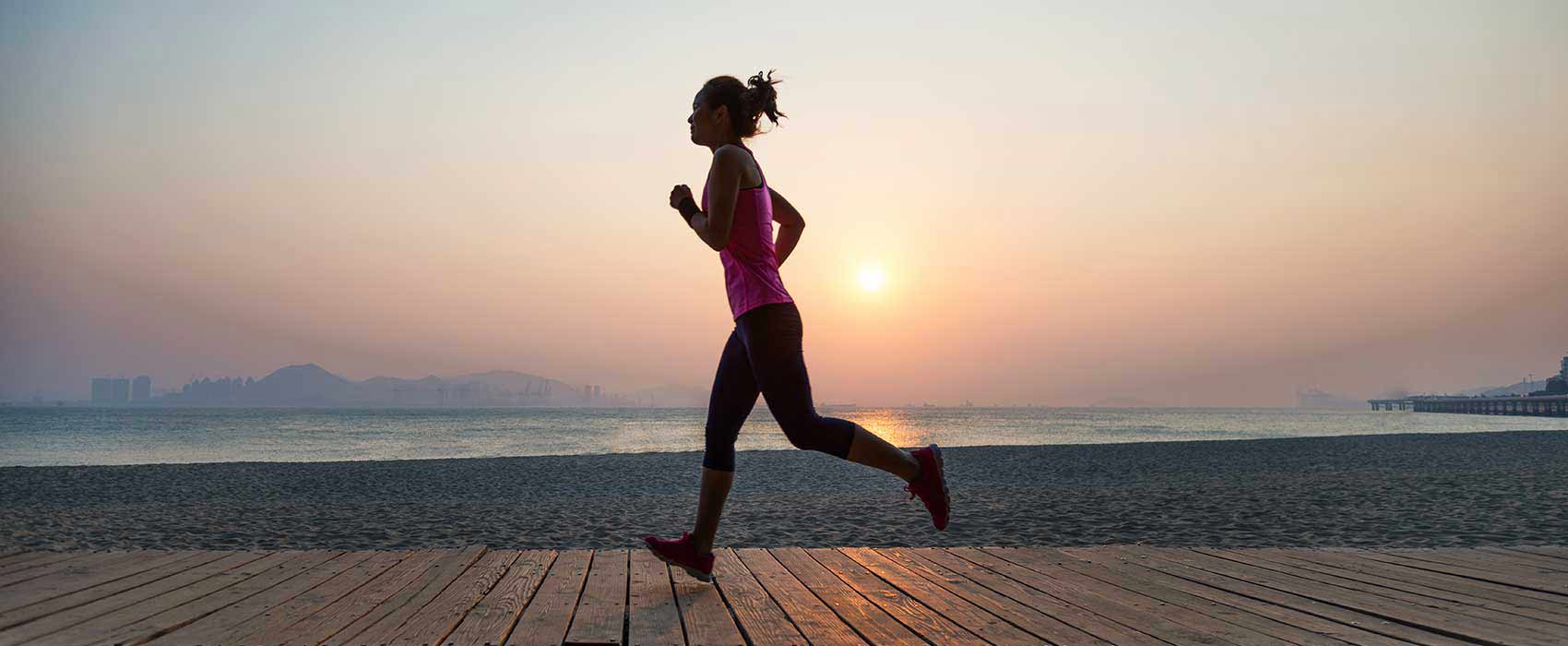 Woman jogging on a boardwalk during sunset.