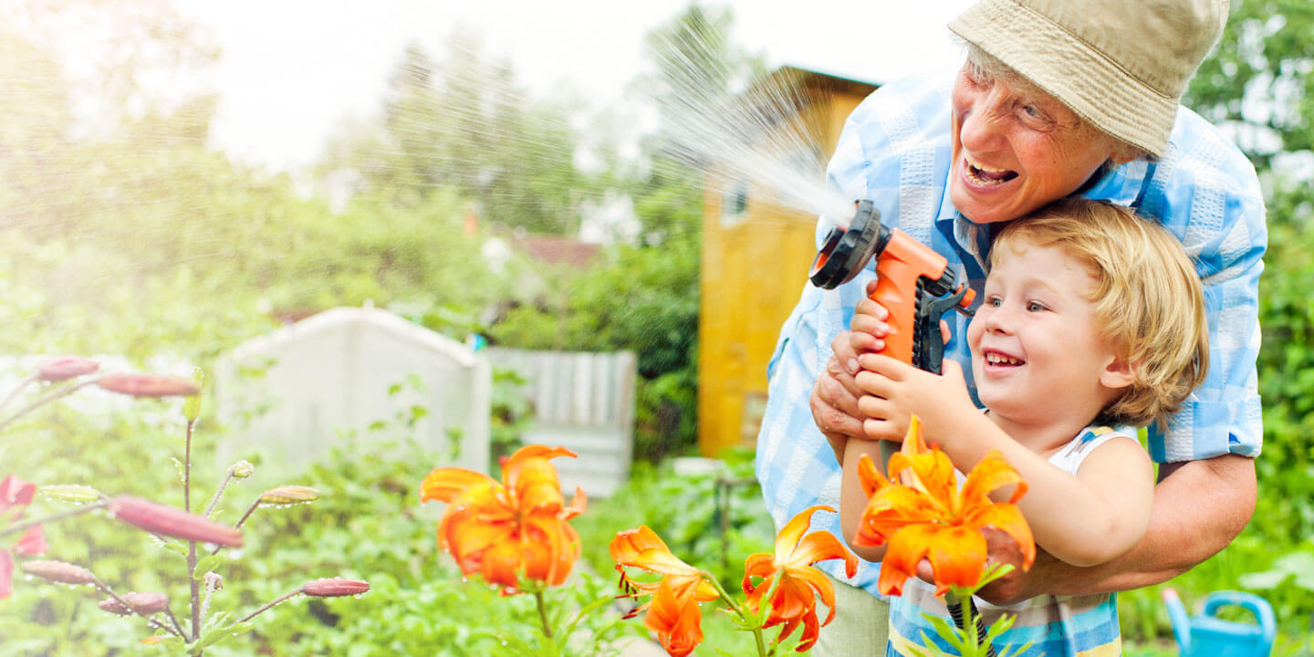 Grandparent with child spraying hose
