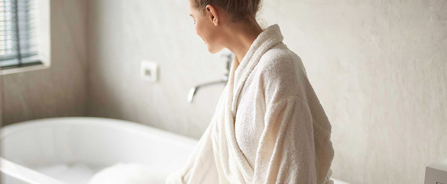 woman in bathrobe sitting beside a tub