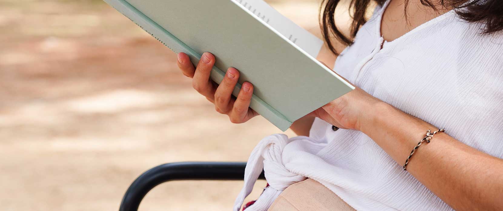 woman reading book outside on bench